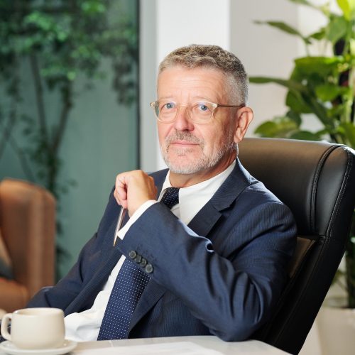 Portrait of middle-aged entrepreneur sitting at office desk with contract and cup of coffee in front of him